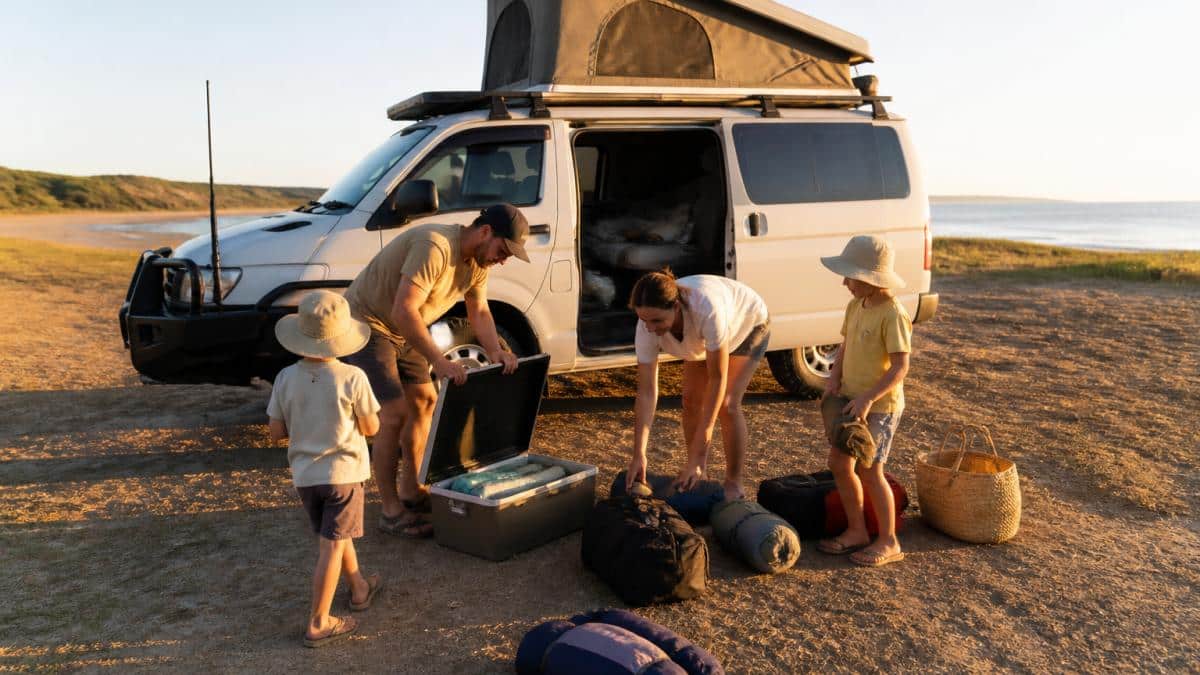 Family of four unpacking gear beside a family friendly campervan hire in Western Australia at a coastal campsite