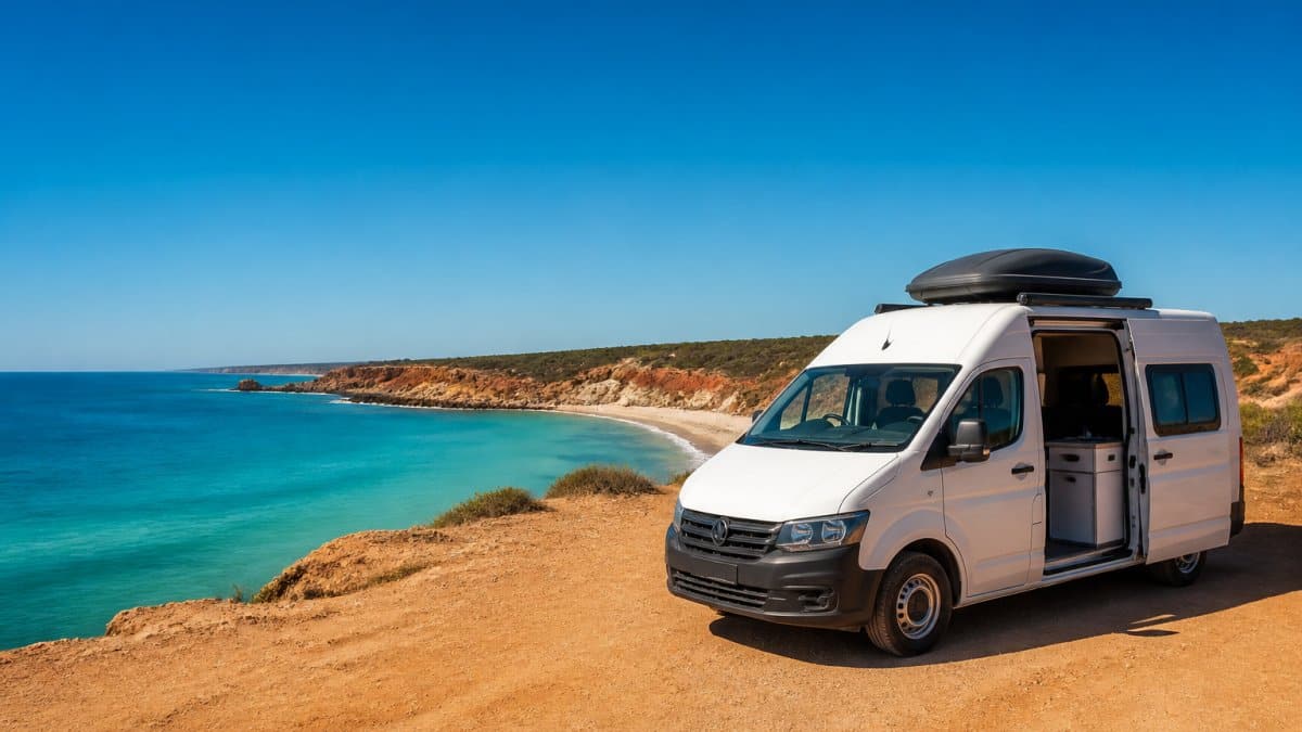 A campervan parked at a scenic coastal viewpoint with turquoise water and red cliffs visible in the background, showcasing the dramatic Western Australian landscape travellers encounter on the Perth to Broome route